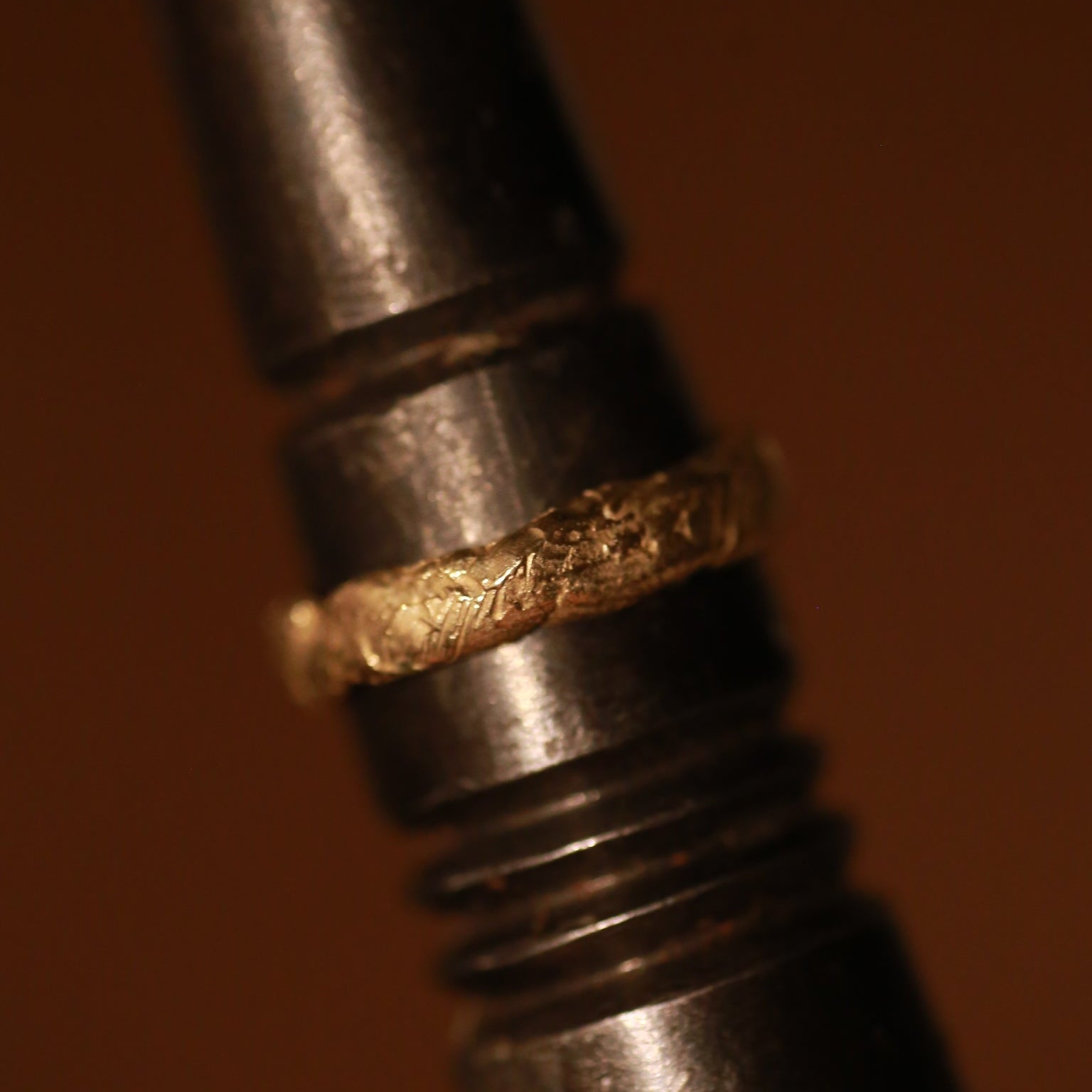 Close-up of a metal object with a gold ring on a brown background