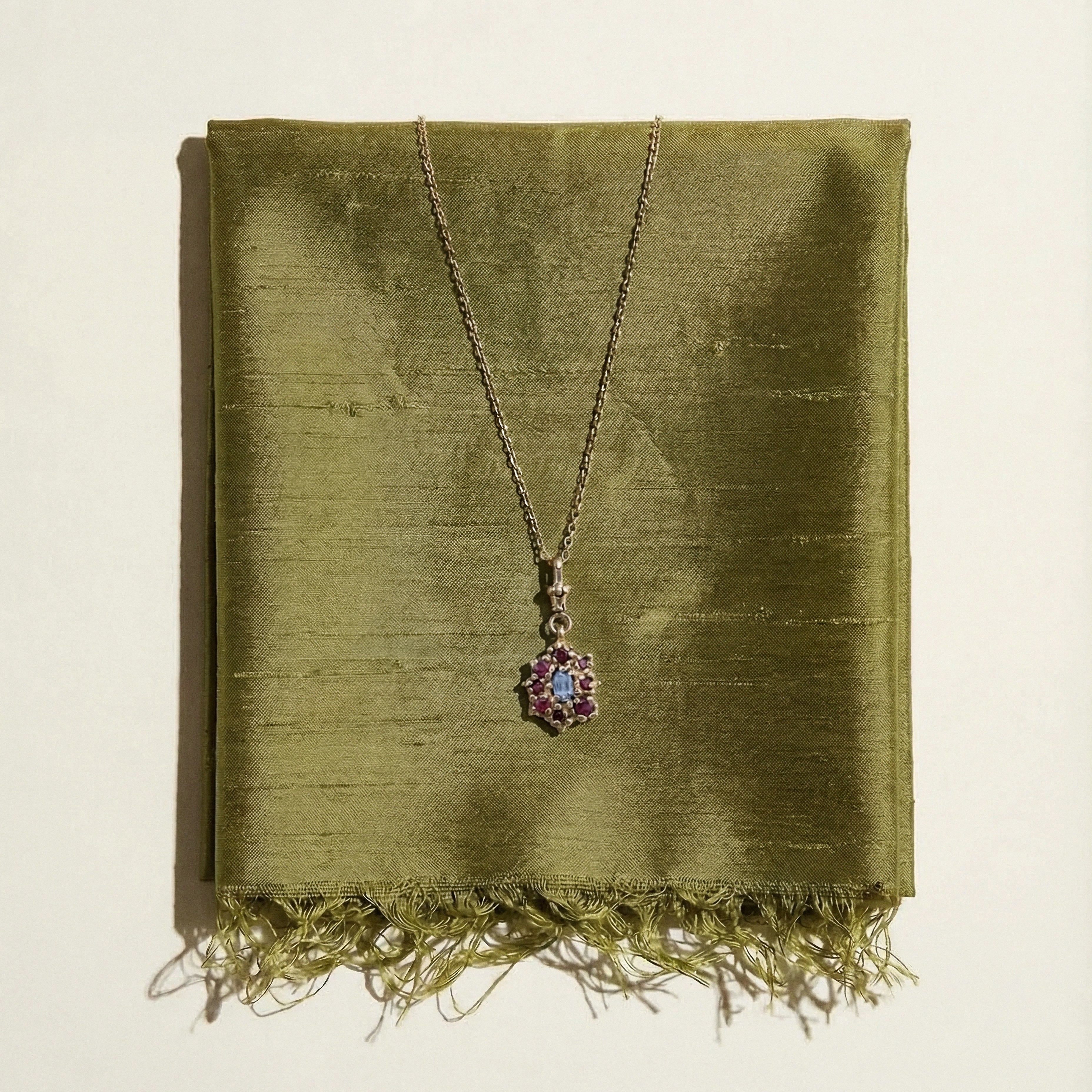 9ct Yellow Gold, victorian inspired, Pendant Necklace, set with a central lilac sapphire and surrounding rubies on a green silk fabric background