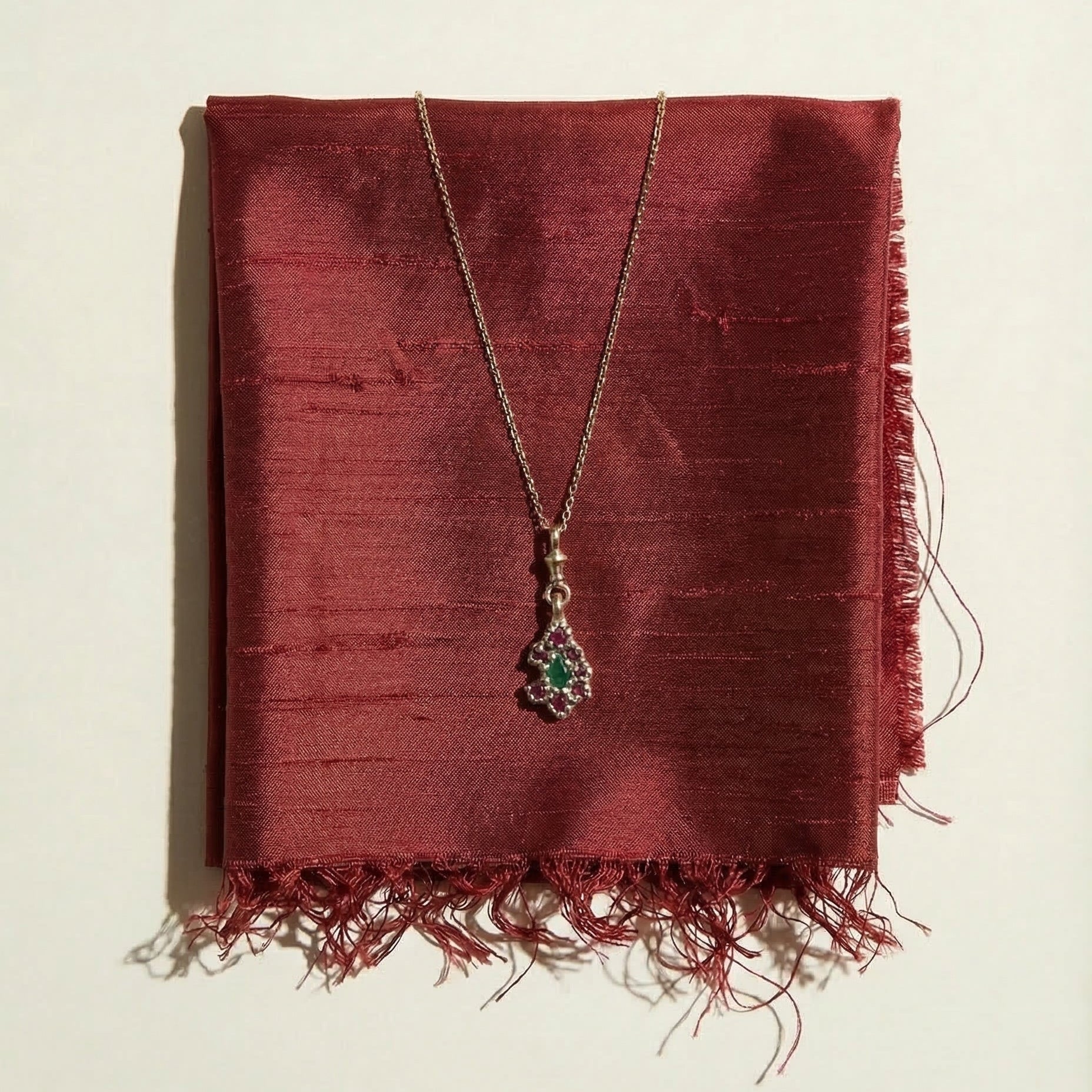 9ct yellow gold victorian inspired pendant Necklace set with central teardrop Emerald and surrounding rubies on a red silk fabric background