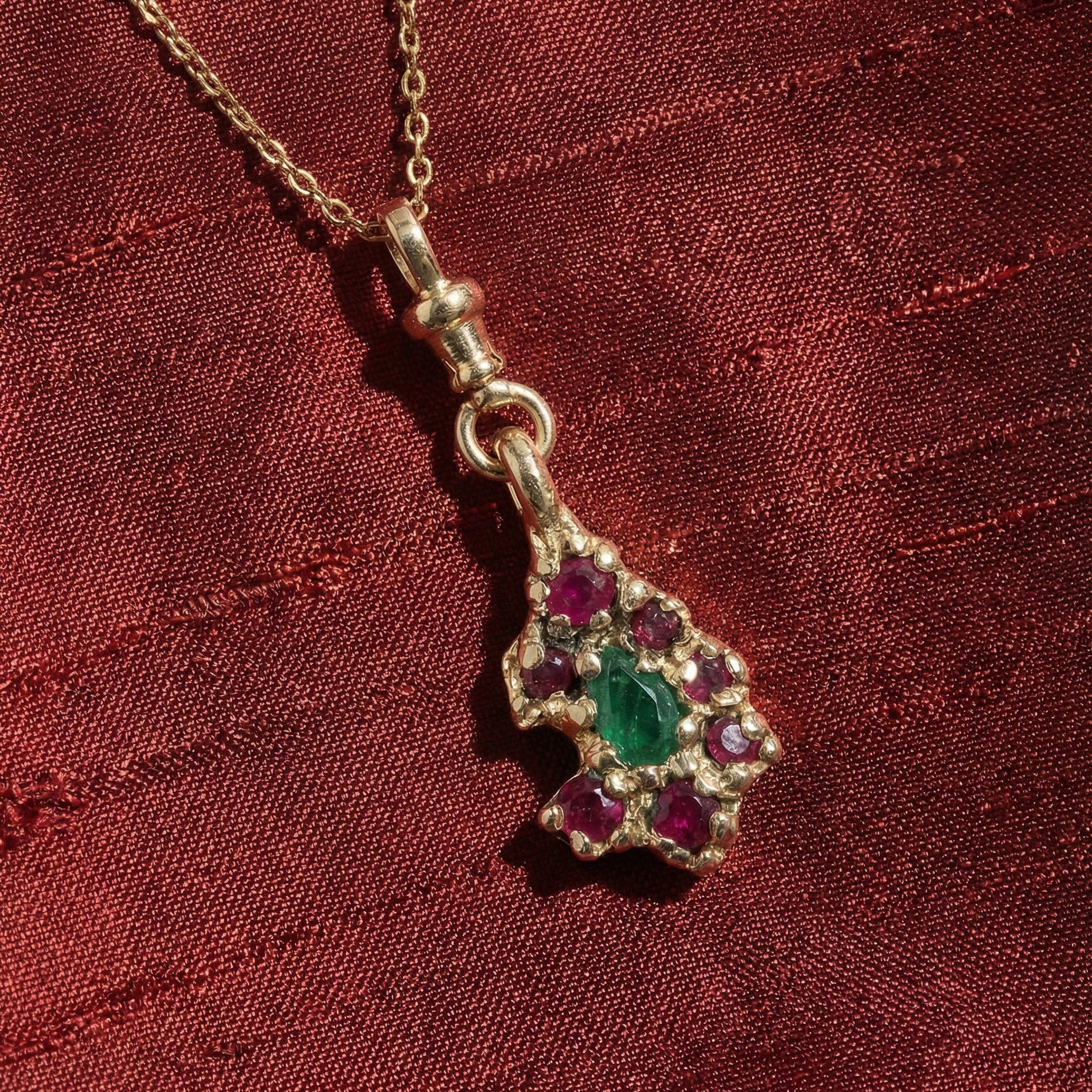 9ct Yellow Gold necklace with a pendant featuring a teardrop emerald and rubies on a red silk fabric background