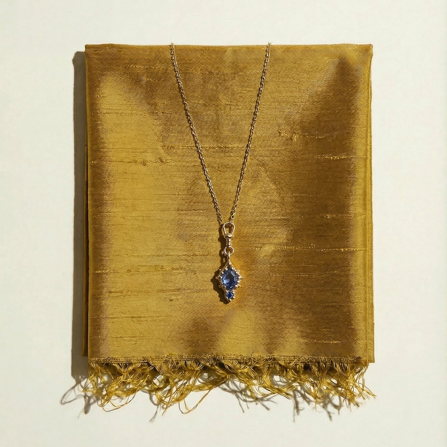 Ancient inspired necklace with a blue Sapphire on a gold fabric background