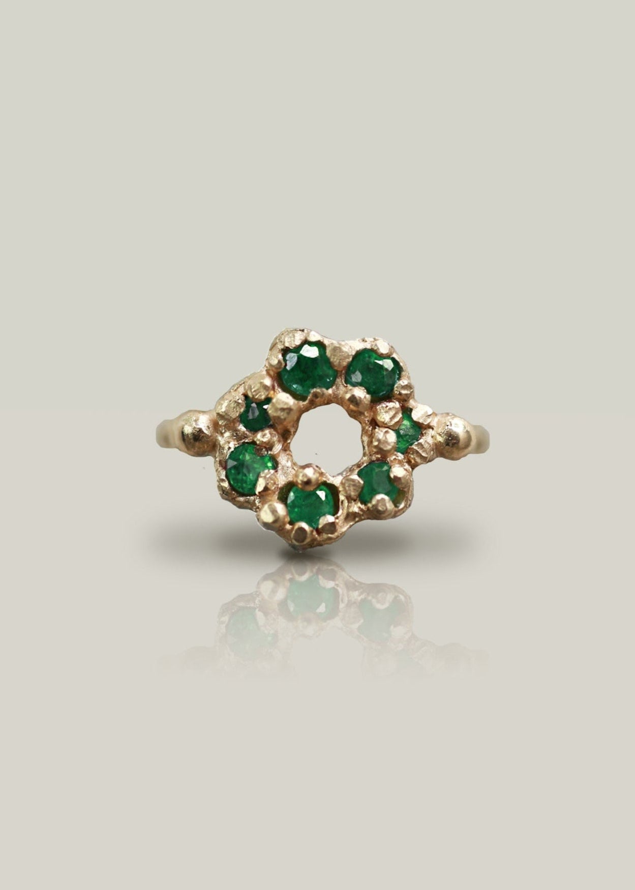 Gold ring with green gemstones on a light gray background