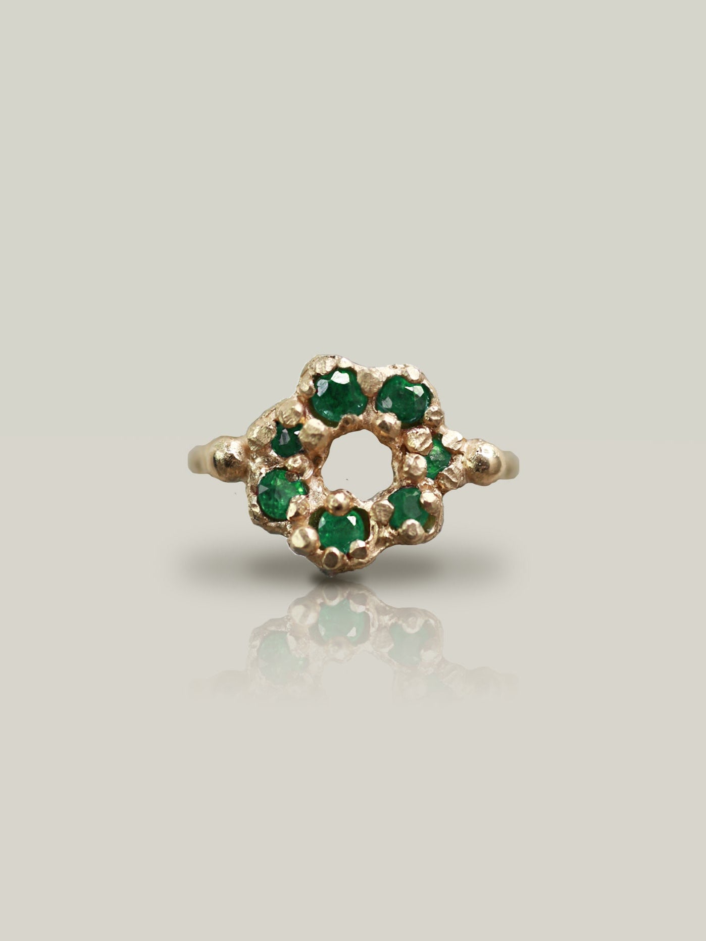 Gold ring with green gemstones on a light gray background