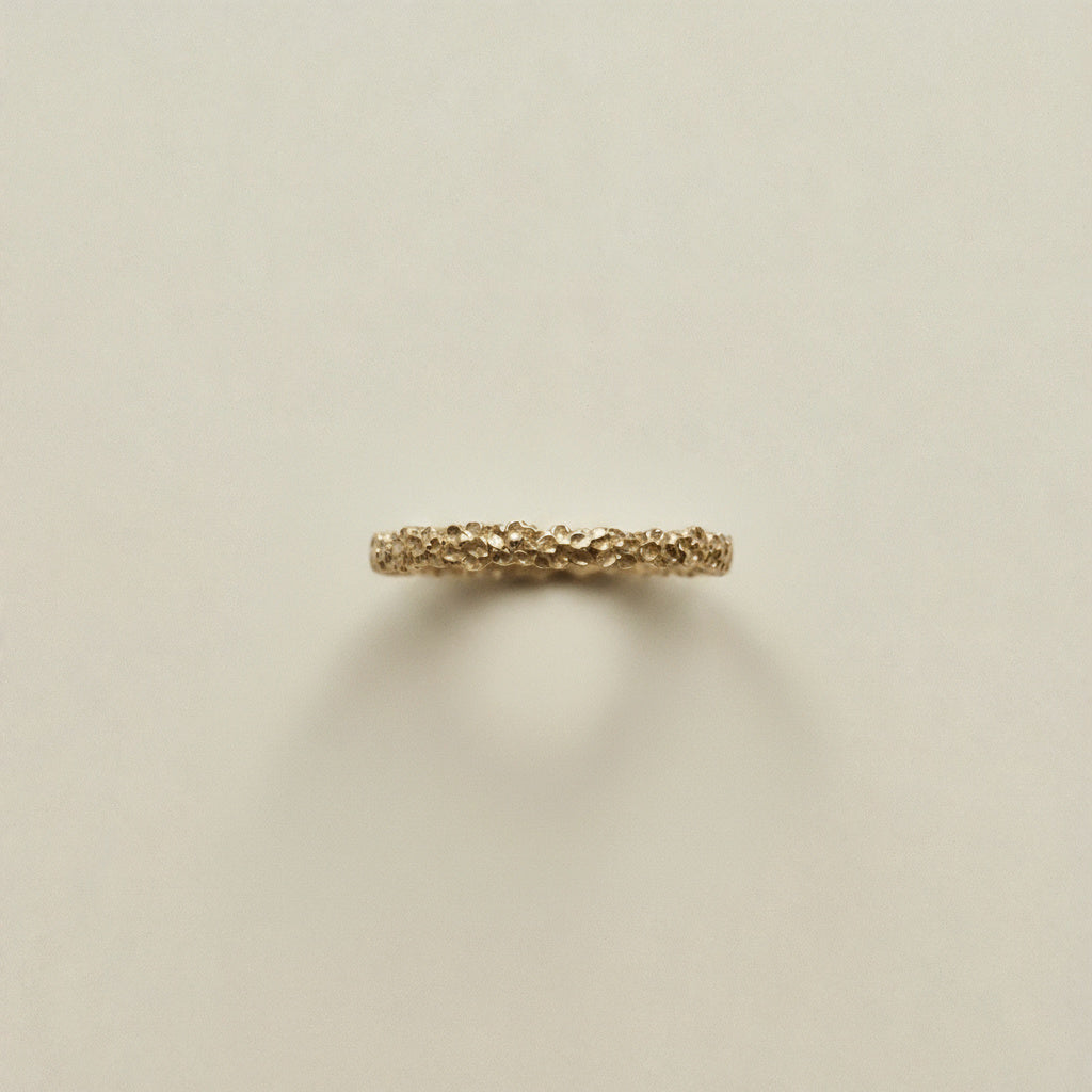 Gold ring with a textured band on a beige background