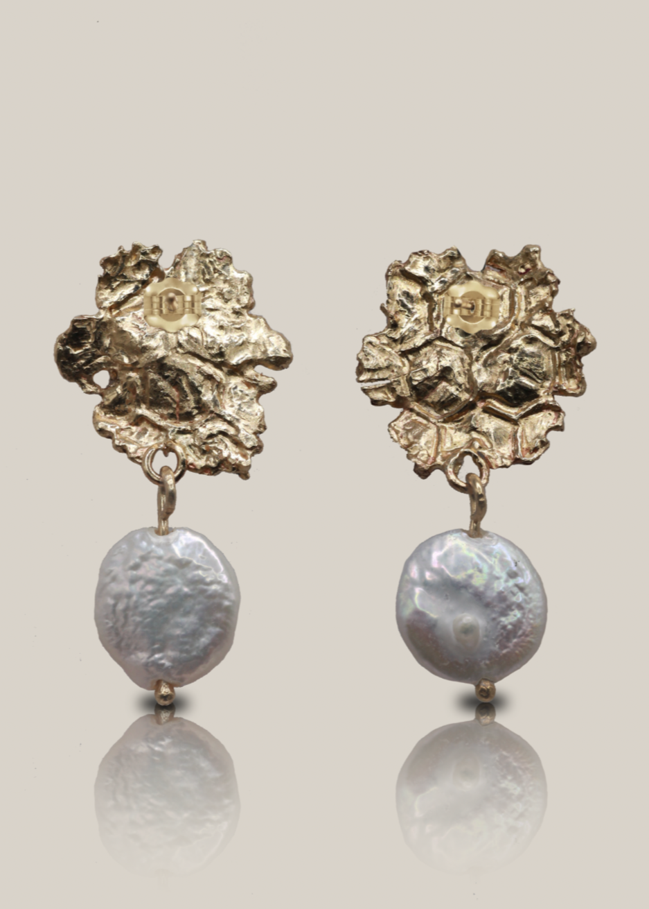 Pair of gold floral earrings with pearl-like beads on a light gray background