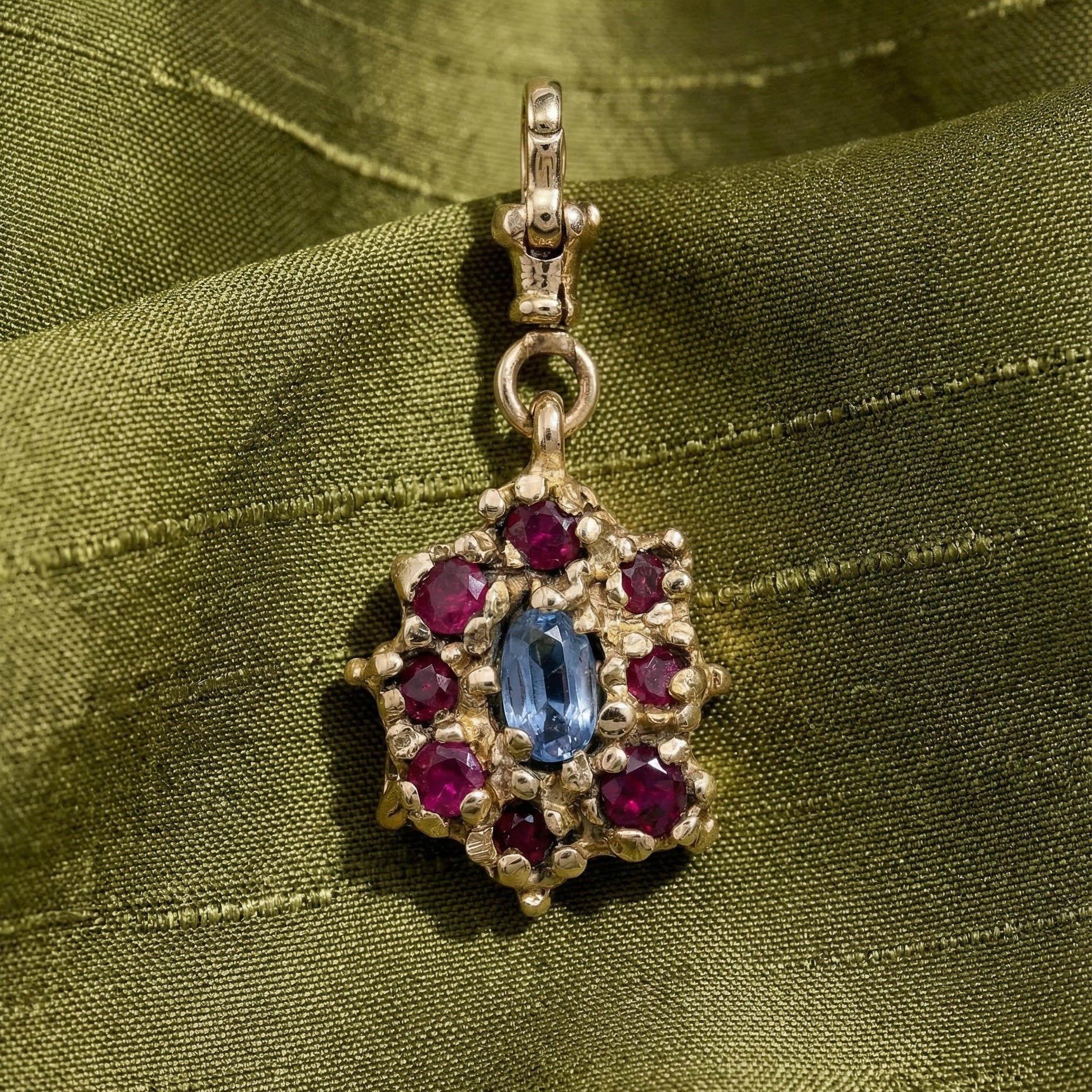 9ct yellow Gold victorian inspired pendant with a central lilac sapphire and surrounding rubies, on a green silk fabric background