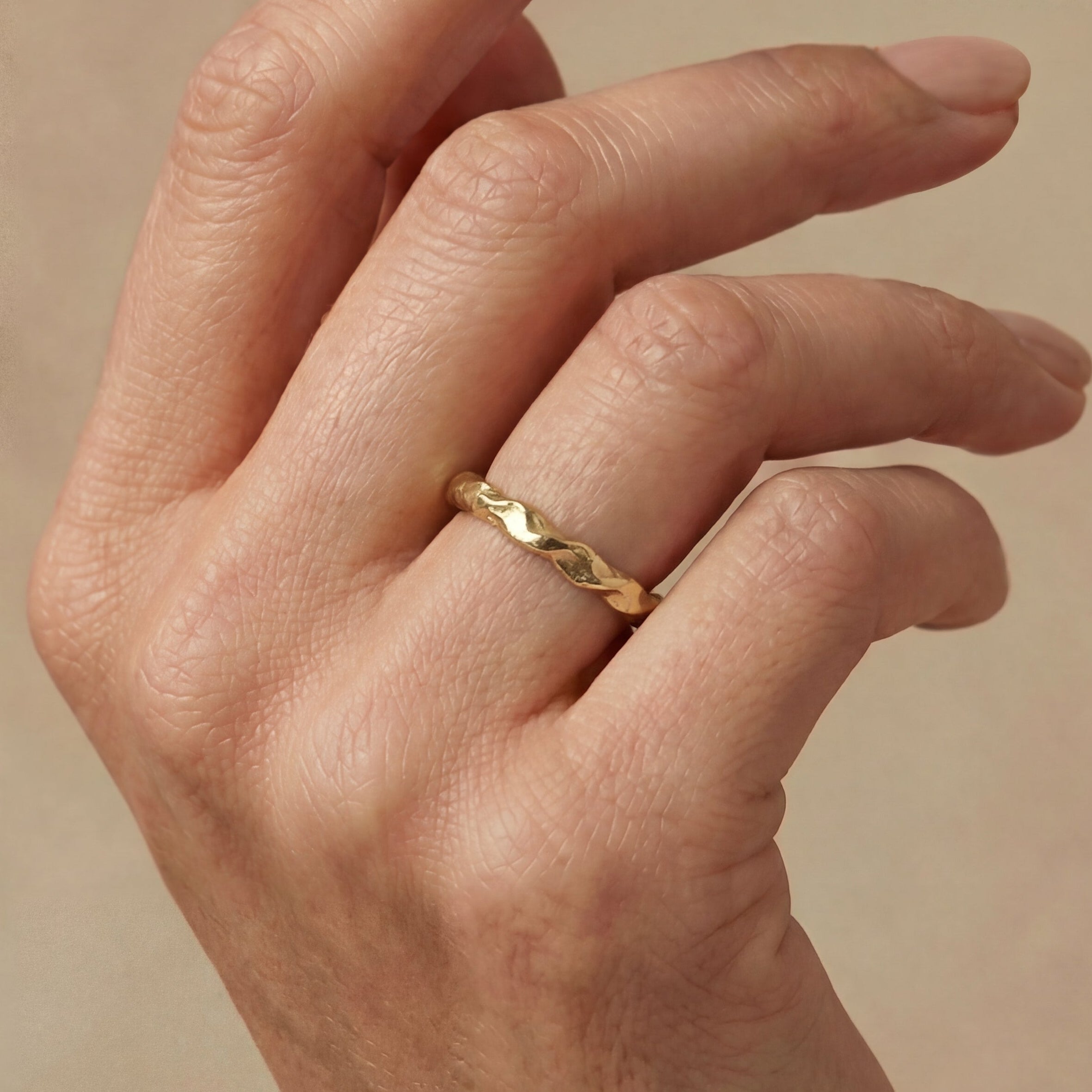 Hand wearing a gold ring on a beige background